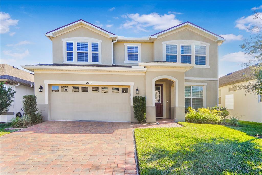 A two-story suburban house with a beige stucco exterior, a brick driveway, and a garage — 2045 SUWANNEE BANKS STREET, CLERMONT, FL