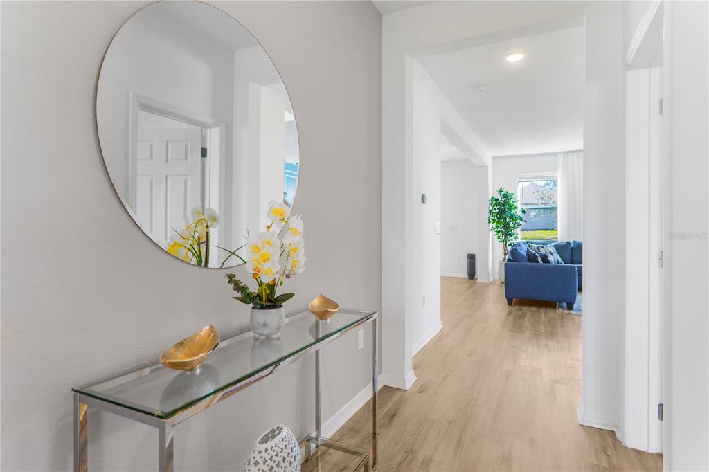 A hallway features a glass console table, a round mirror, and a view into a living room — 2045 SUWANNEE BANKS STREET, CLERMONT, FL