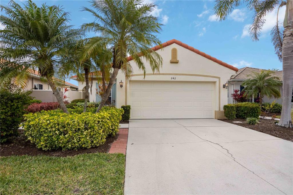 A single-story house with a two-car garage, a tiled roof, and landscaped front yard — 242 MESTRE PLACE, NOKOMIS, FL