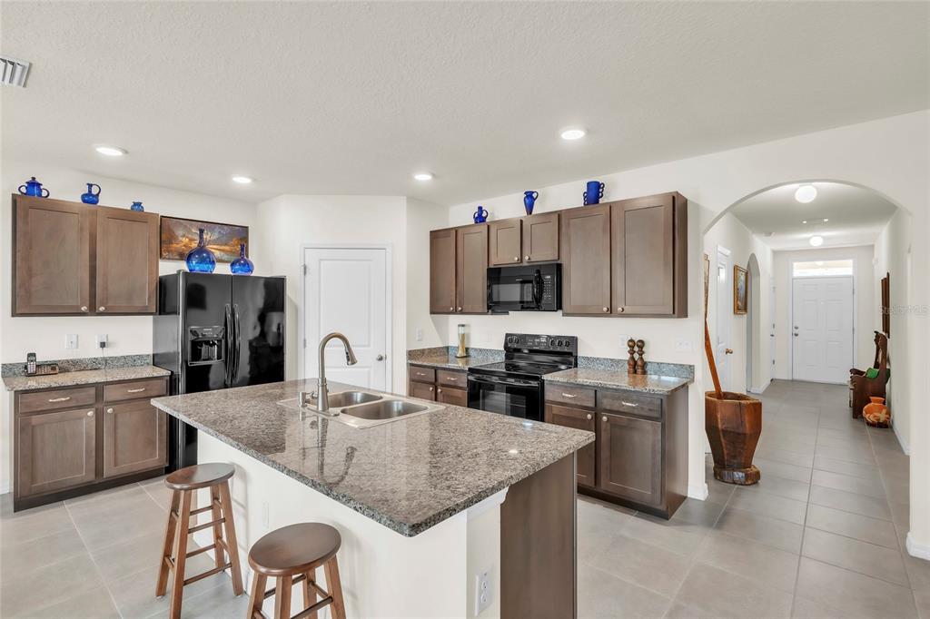 A kitchen with dark wood cabinets, granite countertops, a central island, and tile flooring — 9527 SUNSTONE BOULEVARD, THONOTOSASSA, FL