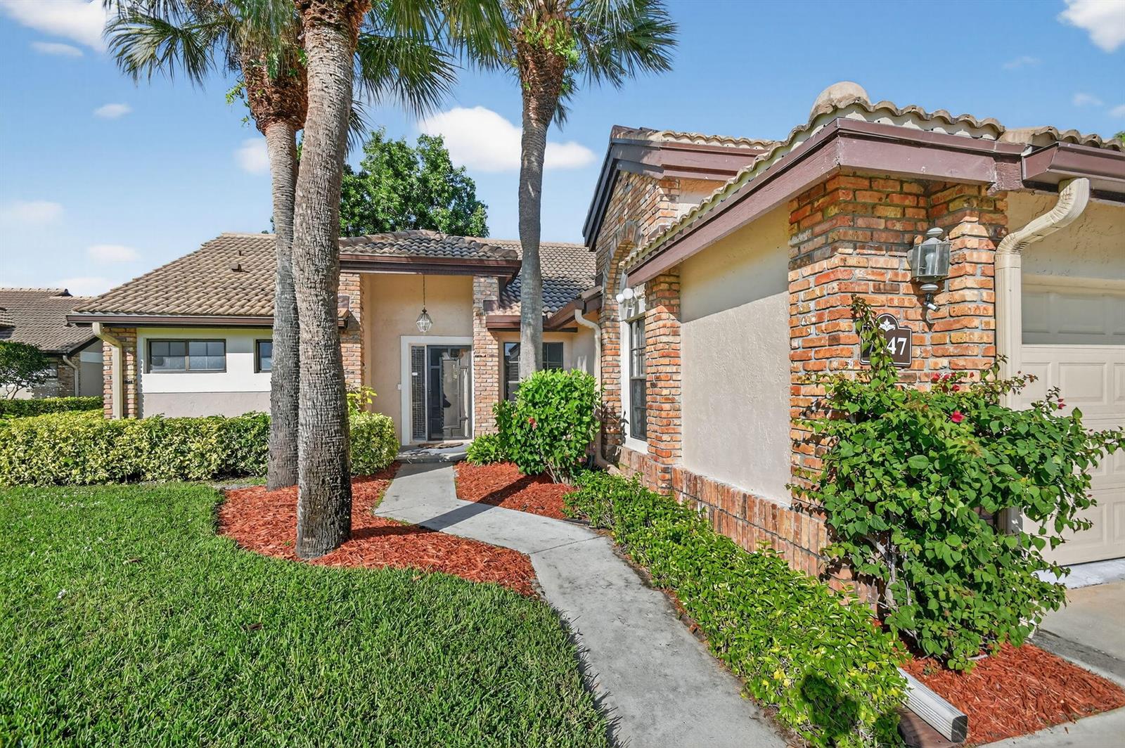 A single-story brick and stucco house features a tiled roof, palm trees, and a walkway — 7147 Le Chalet Boulevard, Boynton Beach FL 33472, BOYNTON BEACH, FL