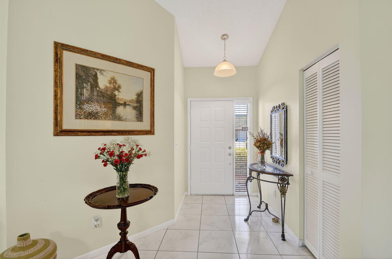 An entryway features light-colored walls, white tile flooring, a front door, and decorative furniture — 7147 Le Chalet Boulevard, Boynton Beach FL 33472, BOYNTON BEACH, FL