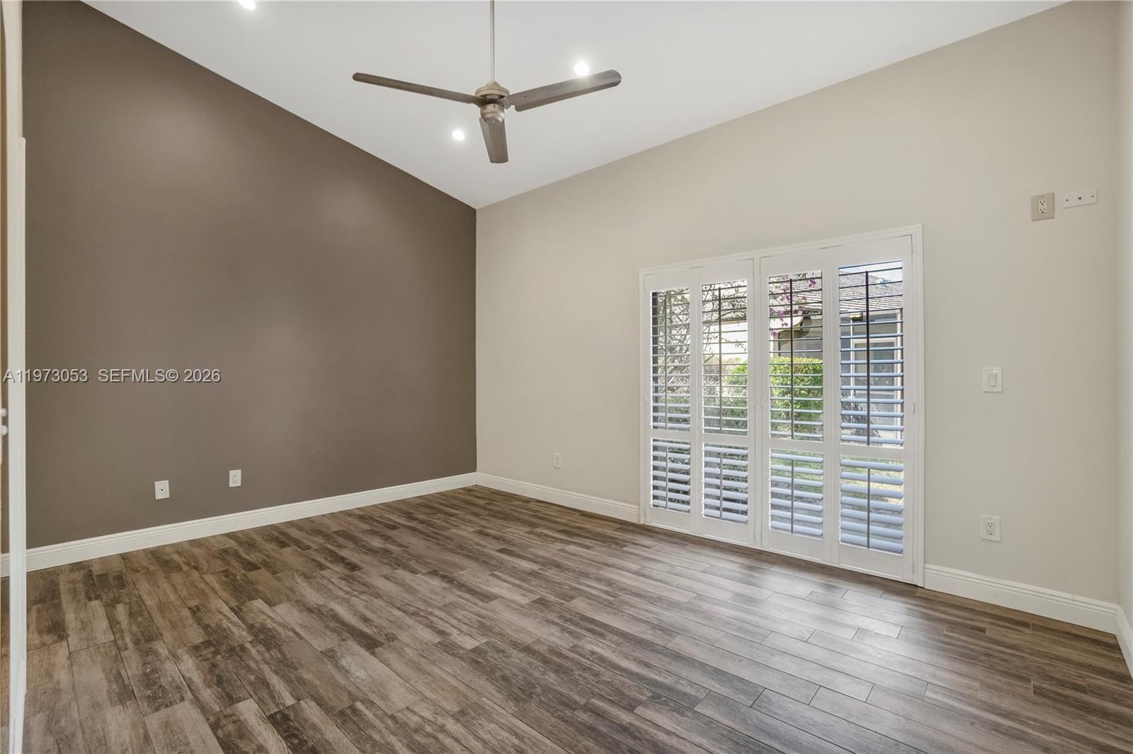 A bedroom features a gray upholstered bed, wood-look flooring, and white plantation shutters on doors — 349 NW 94th Ter, Plantation FL 33324, PLANTATION, FL