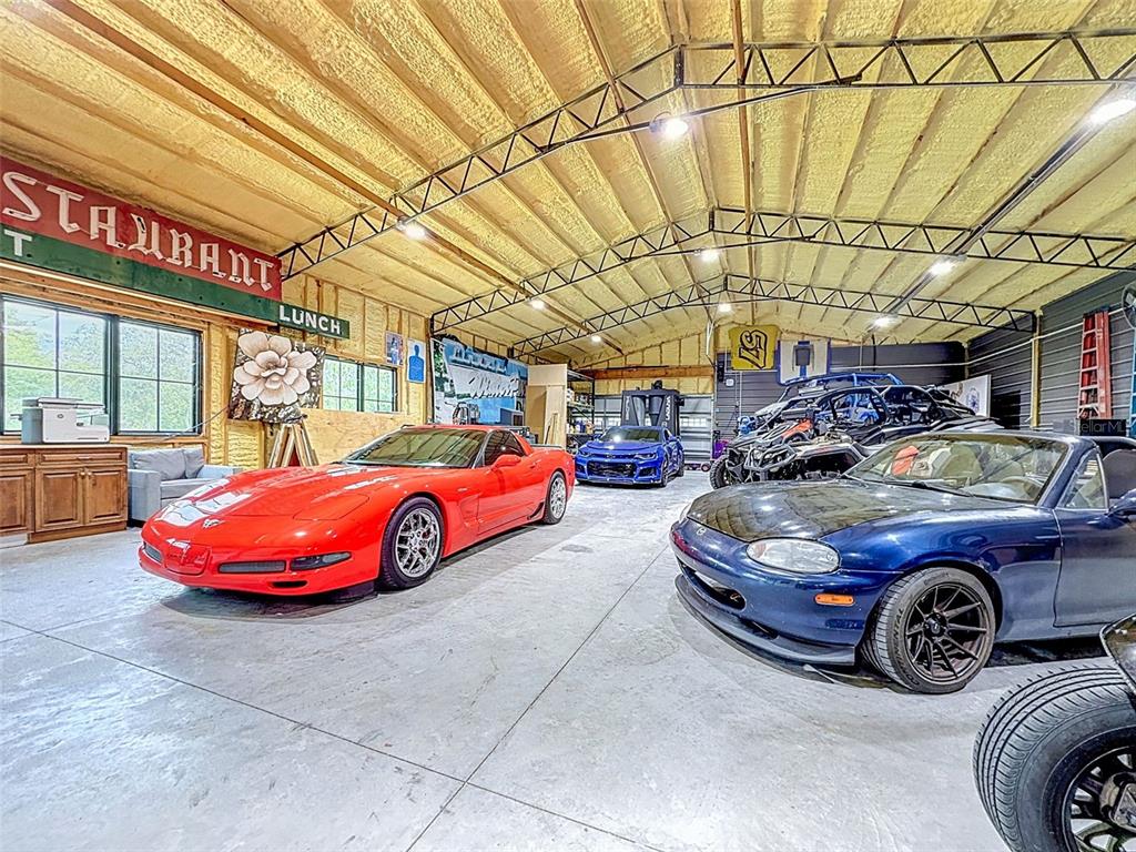 A spacious garage features a concrete floor, exposed metal trusses, and several parked vehicles — 30115 W THYME AVE, EUSTIS, FL