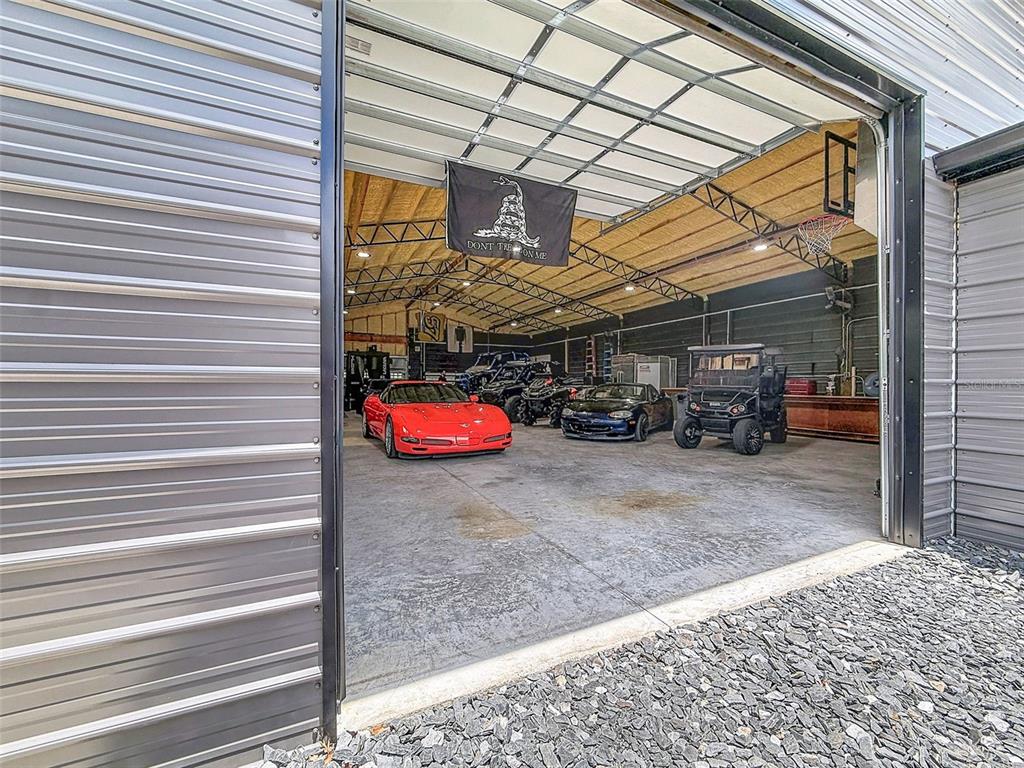 A large metal garage contains a red sports car, a black car, and a golf cart — 30115 W THYME AVE, EUSTIS, FL