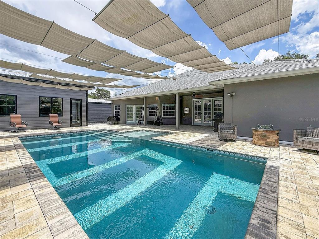 A backyard swimming pool with a sun shade canopy and stone patio area — 30115 W THYME AVE, EUSTIS, FL