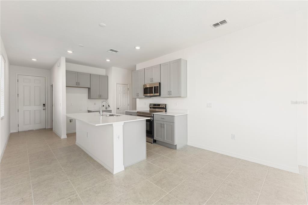 A modern kitchen features light gray cabinets, a white island, and stainless steel appliances — 9116 WILDLIGHT TRAIL, WILDWOOD, FL
