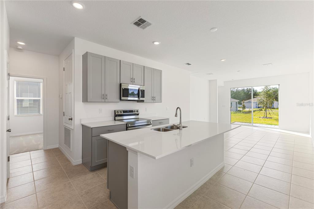 A modern kitchen features gray cabinets, white countertops, a central island, and tile flooring — 9116 WILDLIGHT TRAIL, WILDWOOD, FL