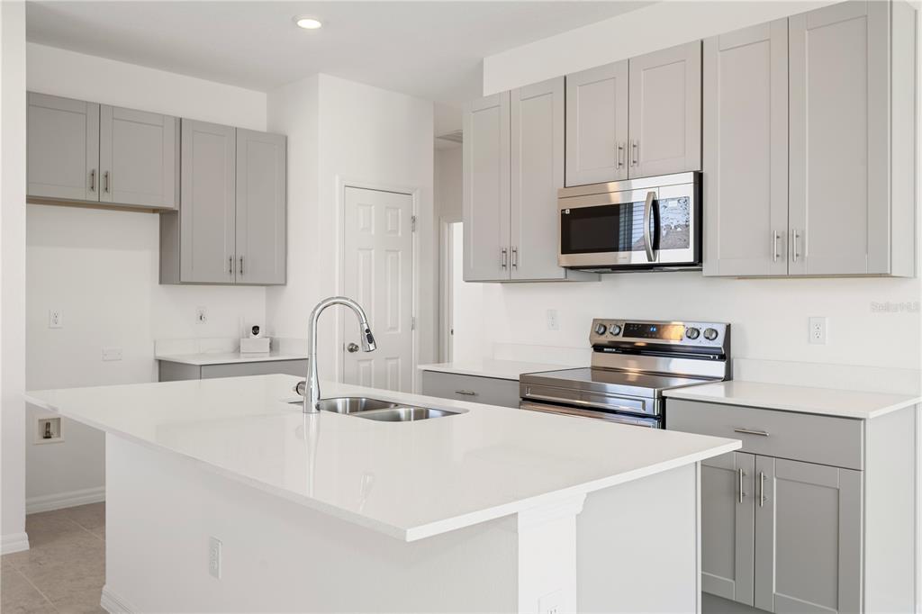 A modern kitchen features light gray cabinets, white countertops, a central island, and stainless steel appliances — 9116 WILDLIGHT TRAIL, WILDWOOD, FL