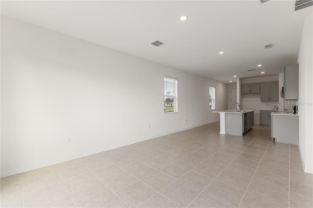 An open-concept kitchen and living area with light tile flooring and grey cabinetry — 9116 WILDLIGHT TRAIL, WILDWOOD, FL