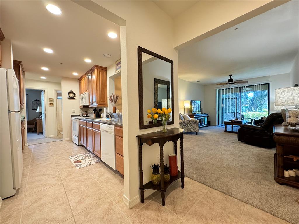 A kitchen with wood cabinets and tile floors opens into a carpeted living room — 7212 HAMILTON ROAD UNIT 7212, BRADENTON, FL