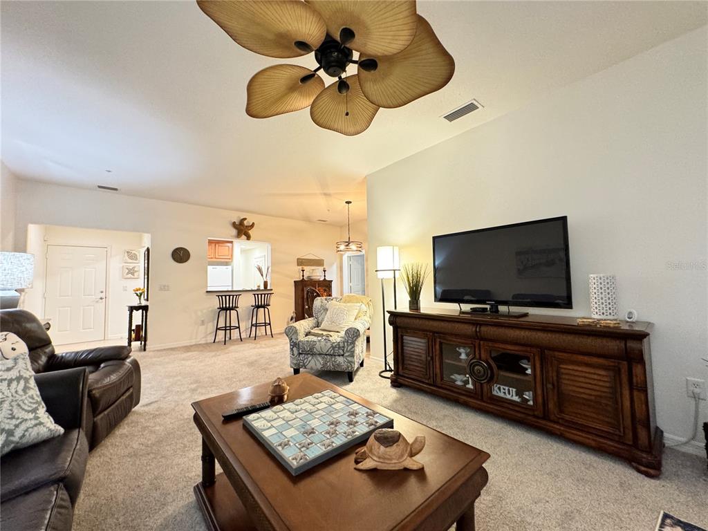 A living room features a ceiling fan, a television on a wooden console, and carpeting — 7212 HAMILTON ROAD UNIT 7212, BRADENTON, FL