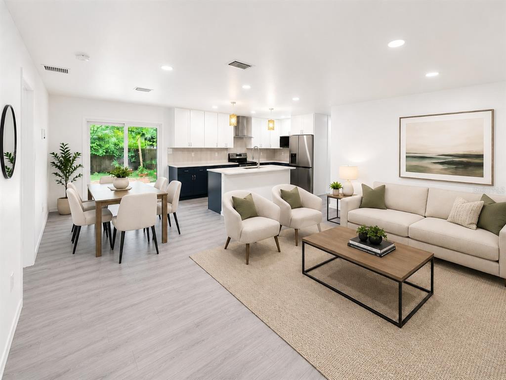 An open-concept kitchen, dining area, and living room featuring white cabinets and light wood flooring — 4302 NW 21ST DRIVE, GAINESVILLE, FL