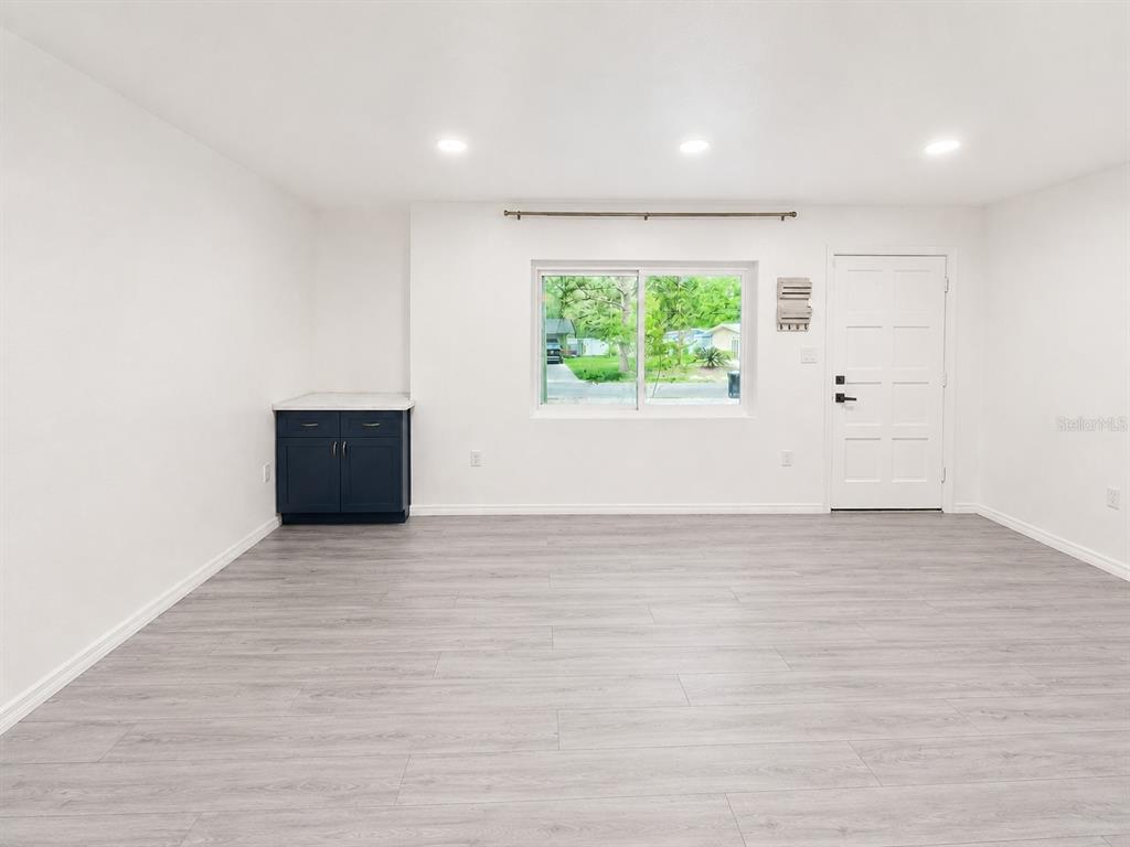 A bright room features light wood-look flooring, white walls, a window, and a dark cabinet — 4302 NW 21ST DRIVE, GAINESVILLE, FL