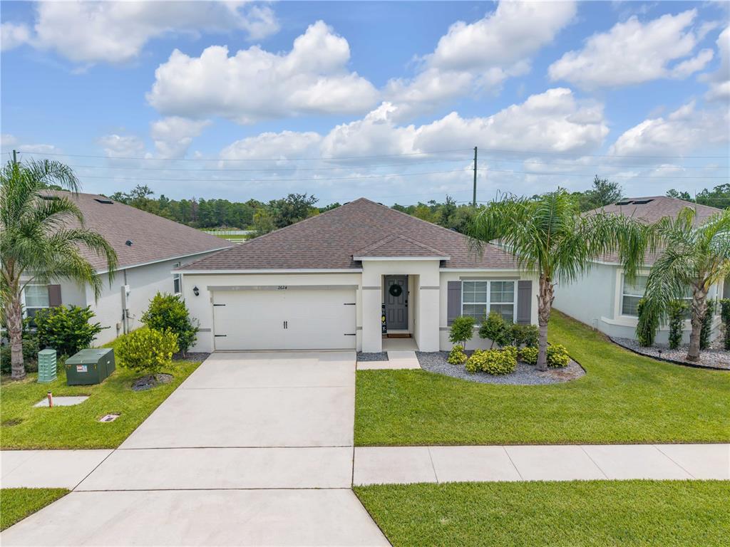 A single-story suburban house with a two-car garage, gray shutters, and palm trees — 2624 NEVERLAND DRIVE, NEW SMYRNA BEACH, FL
