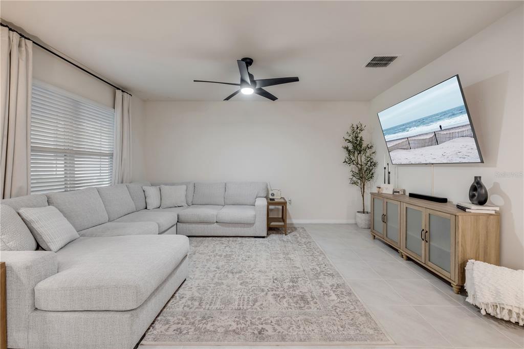 A living room features a light gray sectional sofa, a patterned rug, and a wall-mounted television — 2624 NEVERLAND DRIVE, NEW SMYRNA BEACH, FL