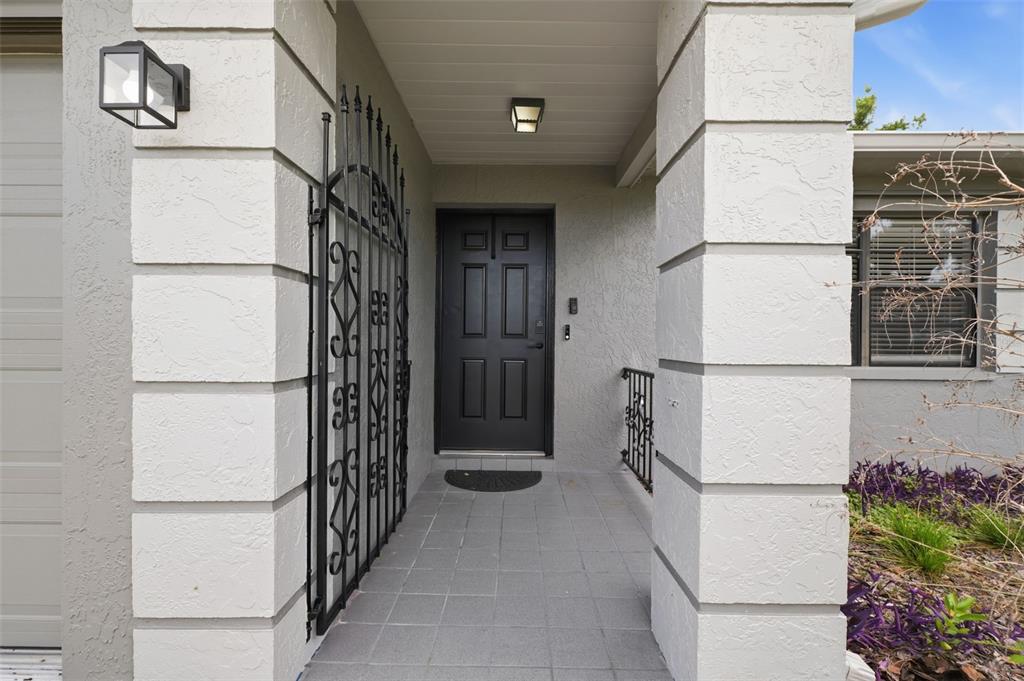 A covered entryway features a black front door, tiled floor, and decorative metal security gates — 6310 GAINSBORO AVENUE, SPRING HILL, FL