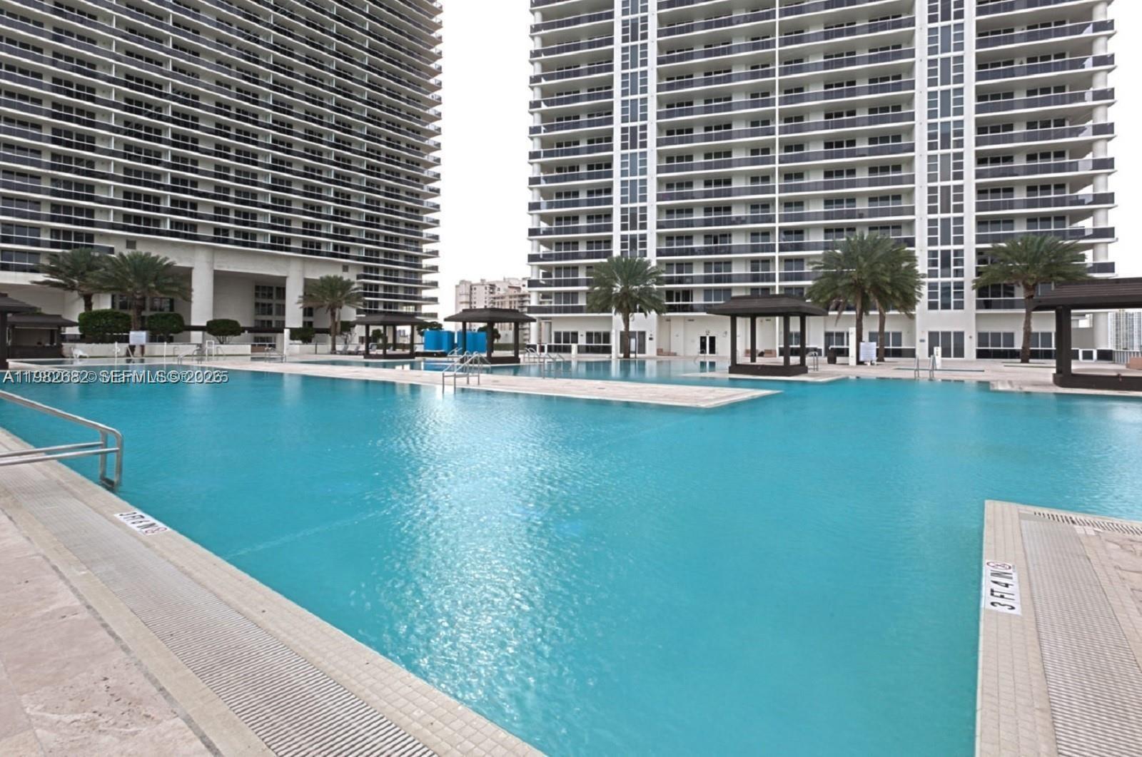 A large swimming pool sits between two tall residential buildings with palm trees and cabanas — 1830 S Ocean Dr # 4608, Hallandale Beach FL 33009, HALLANDALE BEACH, FL