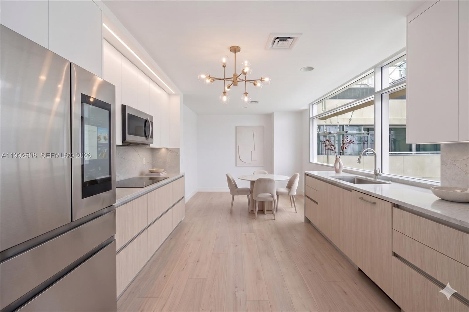 A modern galley kitchen features light wood cabinetry, stainless steel appliances, and an adjacent dining area — 1395 Brickell Ave # 3407, Miami FL 33131, MIAMI, FL