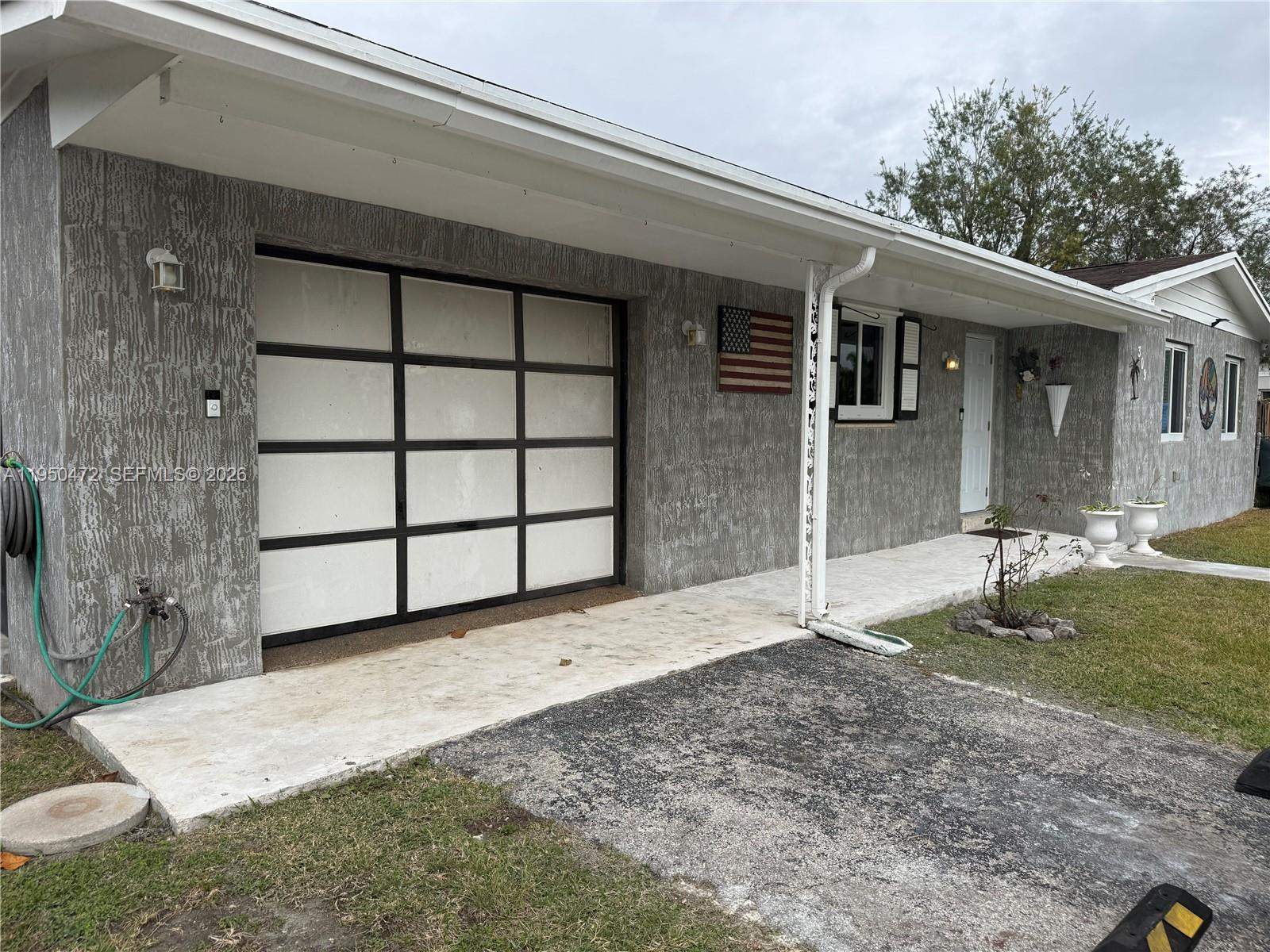 A gray stucco house features a modern glass-paneled garage door and a front porch — 309 NW 15th St, Homestead FL 33030, HOMESTEAD, FL
