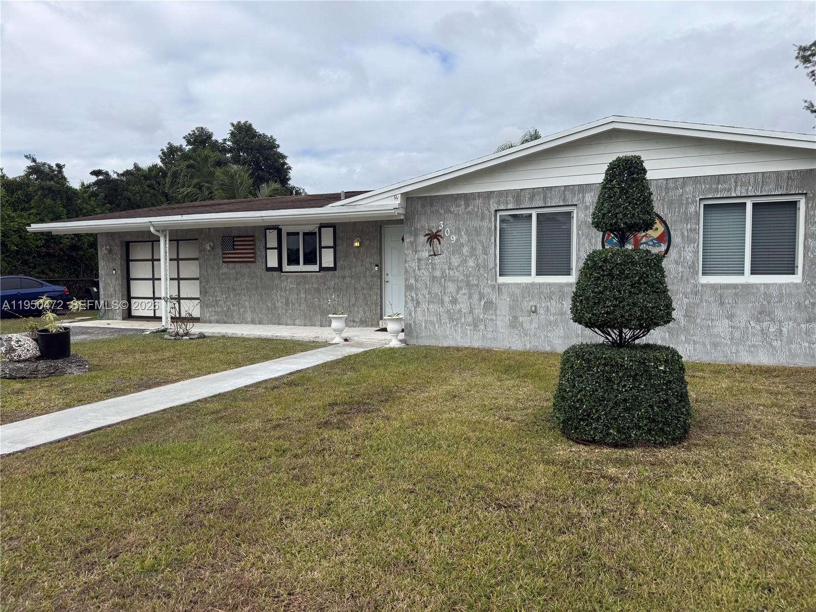 A single-story house with gray textured siding, a white front door, and a topiary tree — 309 NW 15th St, Homestead FL 33030, HOMESTEAD, FL