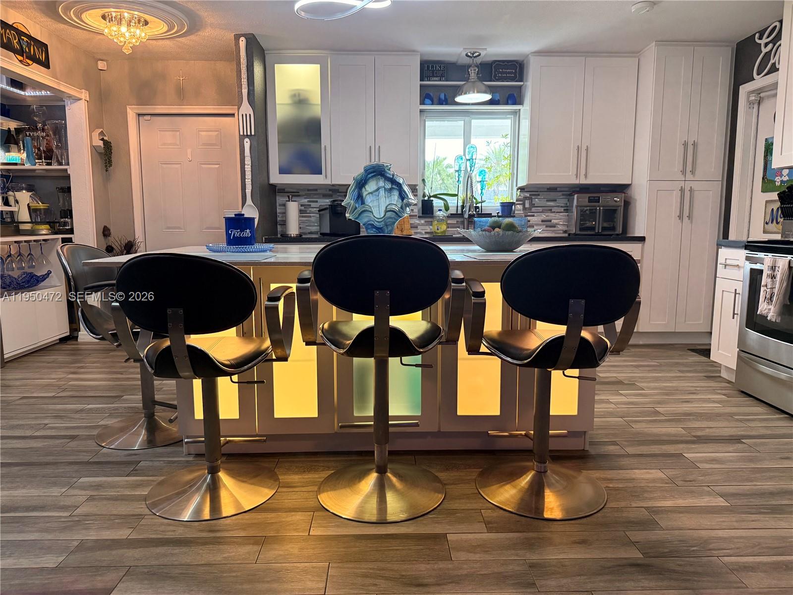 A kitchen features a central island with illuminated panels, three bar stools, and white cabinetry — 309 NW 15th St, Homestead FL 33030, HOMESTEAD, FL