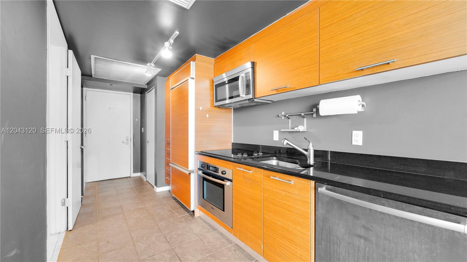 A kitchen features wood-grain cabinets, black countertops, stainless steel appliances, and a tiled floor — 50 Biscayne Blvd # 4203, Miami FL 33132, MIAMI, FL