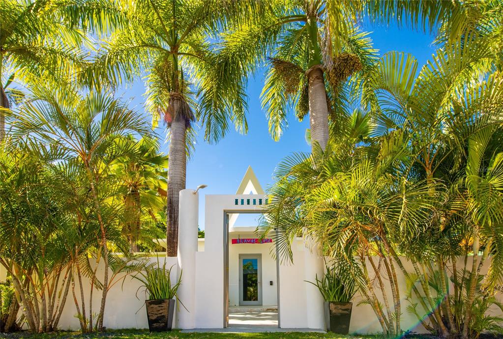 A white gated entrance with a triangular architectural detail is surrounded by lush palm trees — 300 PALM COTTAGES, VIEQUES, PR