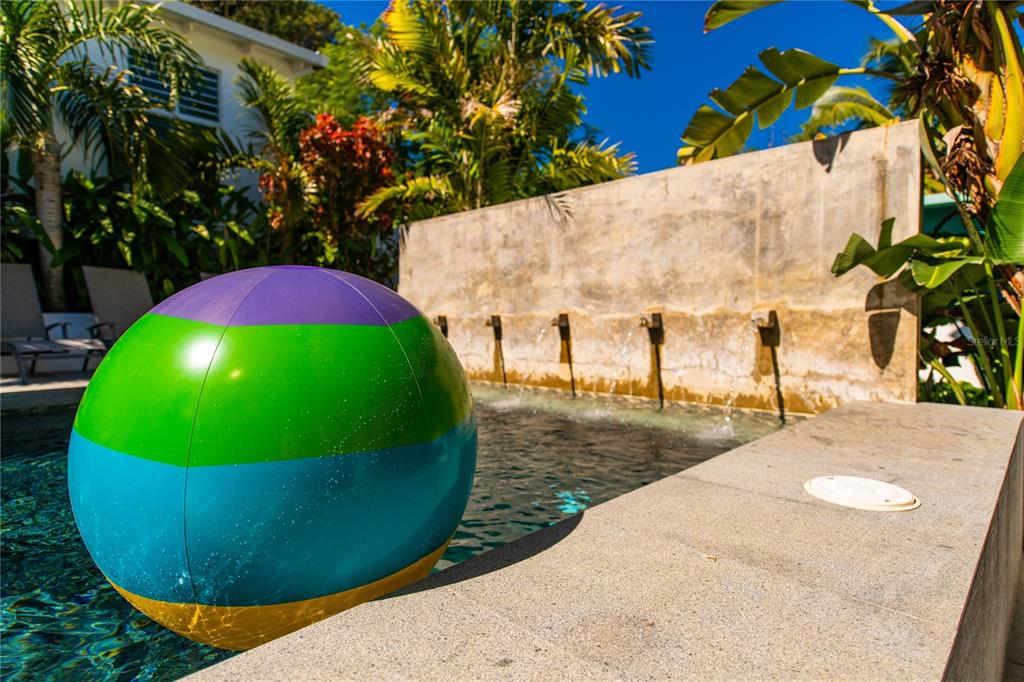 A colorful beach ball floats in a swimming pool with a concrete water feature wall — 300 PALM COTTAGES, VIEQUES, PR