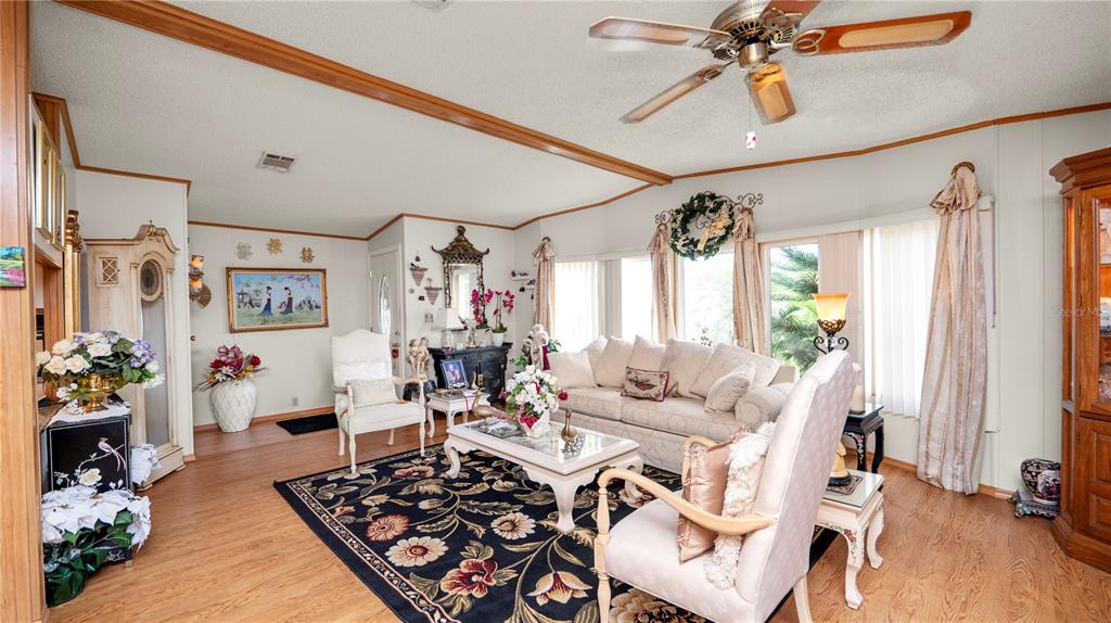An empty living room features light wood-look flooring, white walls, and a ceiling fan — 1706 FOX HILL DRIVE, LAKELAND, FL