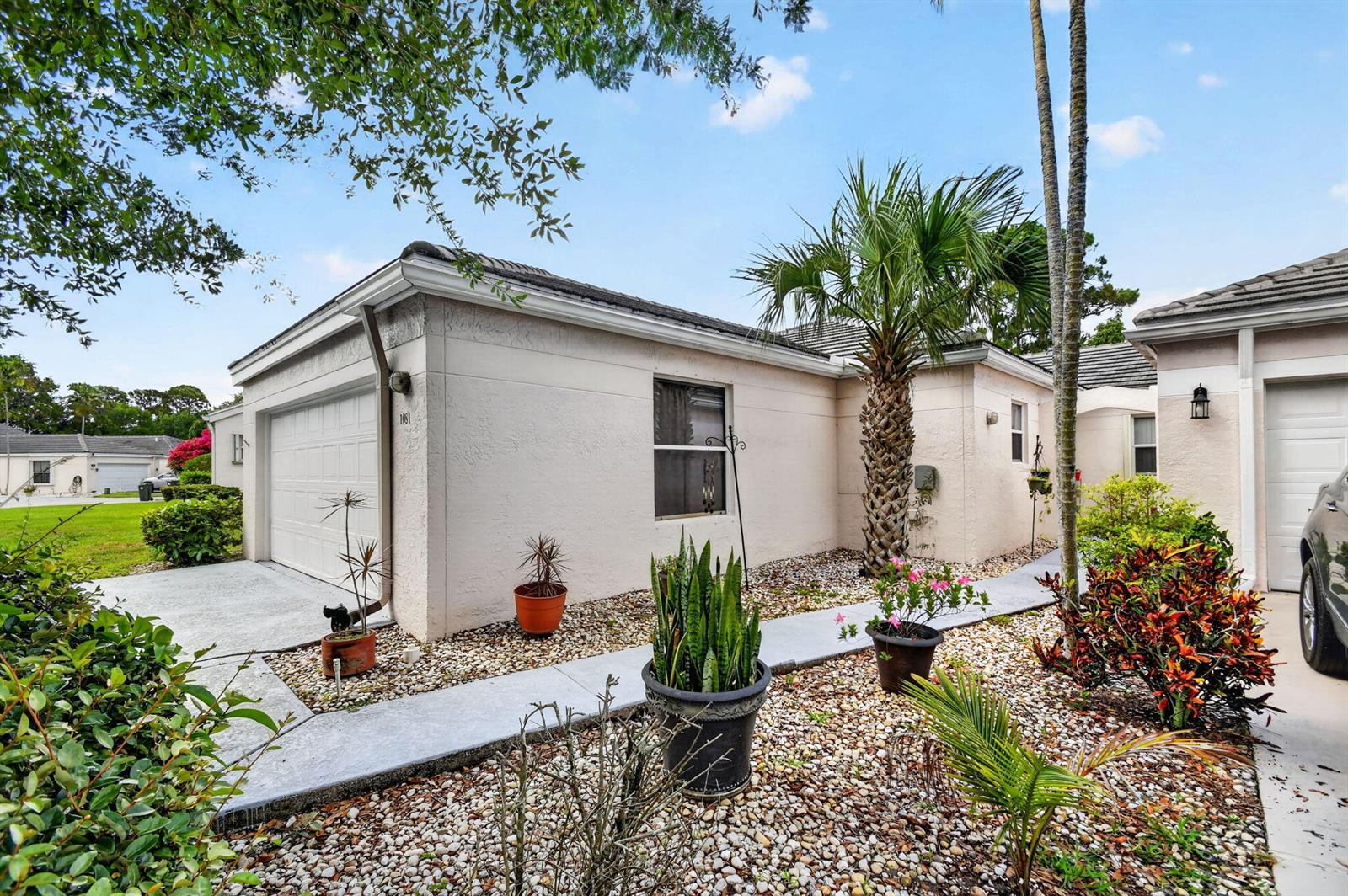 A light-colored house exterior features a garage, a palm tree, and a gravel front yard — 1081 Island Manor Drive, FL 33413, FL