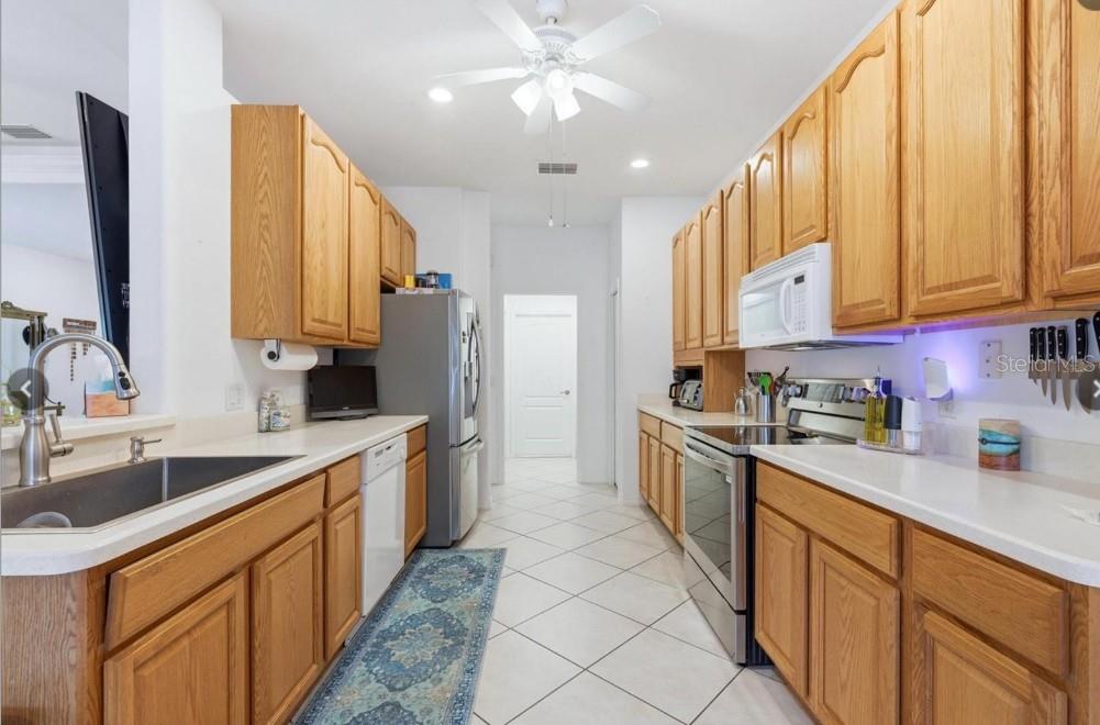 A galley kitchen features oak cabinets, white countertops, stainless steel appliances, and tiled flooring — 5948 ORCHIS ROAD, VENICE, FL