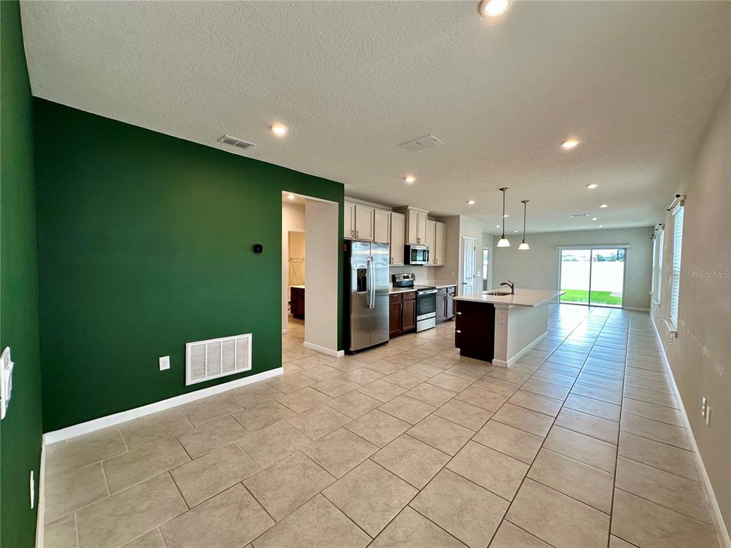 An open-concept kitchen and dining area feature tile flooring, white cabinets, and a green wall — 1528 EUCALYPTUS WAY, DAVENPORT, FL
