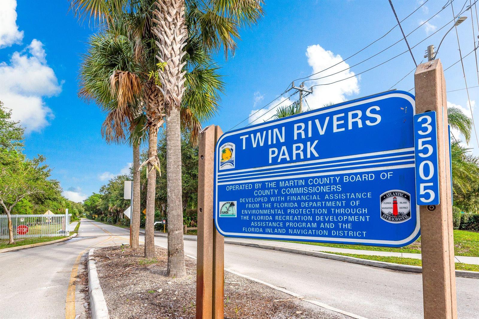 A blue sign for Twin Rivers Park stands beside a paved road with palm trees — 4796 SE Manatee Terrace, Stuart FL 34997, STUART, FL