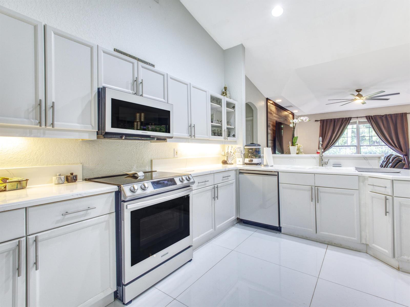 A modern kitchen features white cabinets, stainless steel appliances, and white tile flooring — 6660 Conch Court, Boynton Beach FL 33437, BOYNTON BEACH, FL