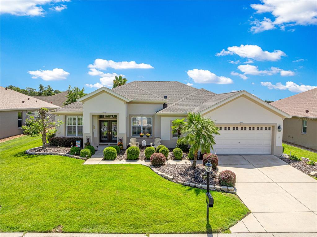 A single-story suburban house with a tan stucco exterior, a two-car garage, and landscaped lawn — 11855 SE 91ST CIRCLE, SUMMERFIELD, FL