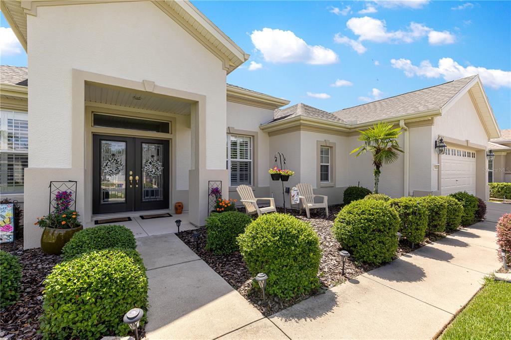 A beige single-story house features a double front door, a concrete walkway, and manicured landscaping — 11855 SE 91ST CIRCLE, SUMMERFIELD, FL