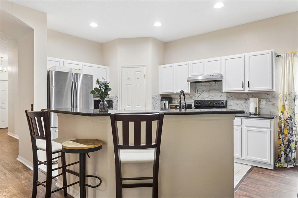A kitchen features white cabinets, dark countertops, stainless steel appliances, and two bar stools — 2925 BANYAN HILL LANE, LAND O LAKES, FL