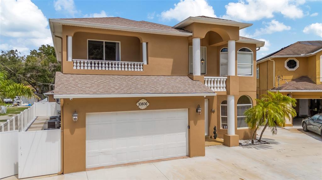 A two-story tan stucco house with a white garage door and a second-floor balcony — 10806 PEREZ DRIVE, TAMPA, FL