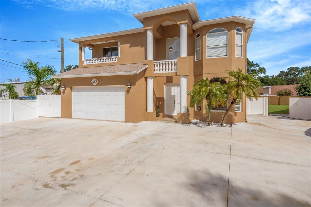 A two-story tan house with a large concrete driveway, a two-car garage, and columns — 10806 PEREZ DRIVE, TAMPA, FL