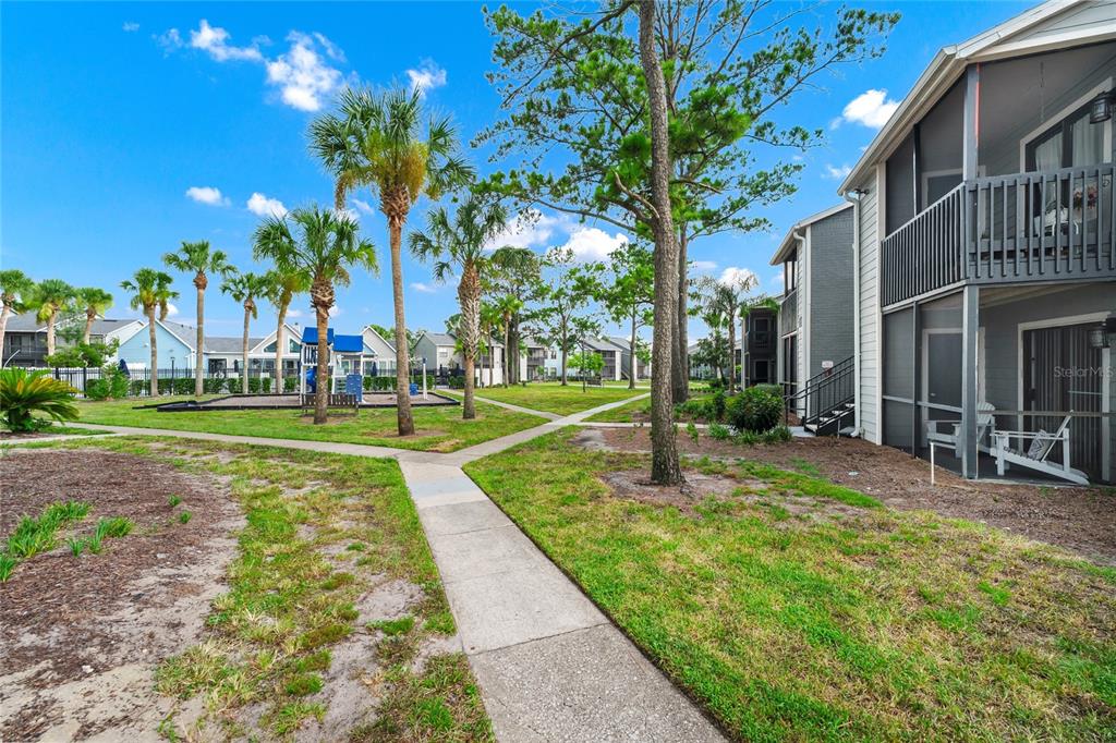 A paved walkway leads through a grassy courtyard with palm trees and a small playground — 3740 IDLEBROOK CIRCLE UNIT 102, CASSELBERRY, FL