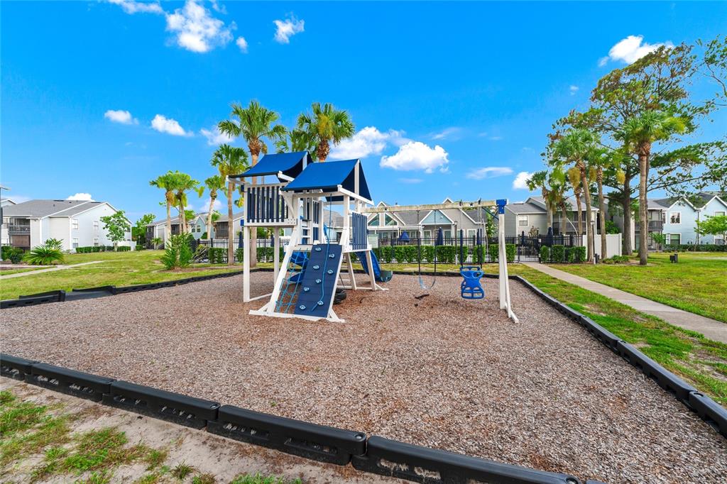 A playground with a climbing structure and swings sits on a wood-chipped lot outdoors — 3740 IDLEBROOK CIRCLE UNIT 102, CASSELBERRY, FL