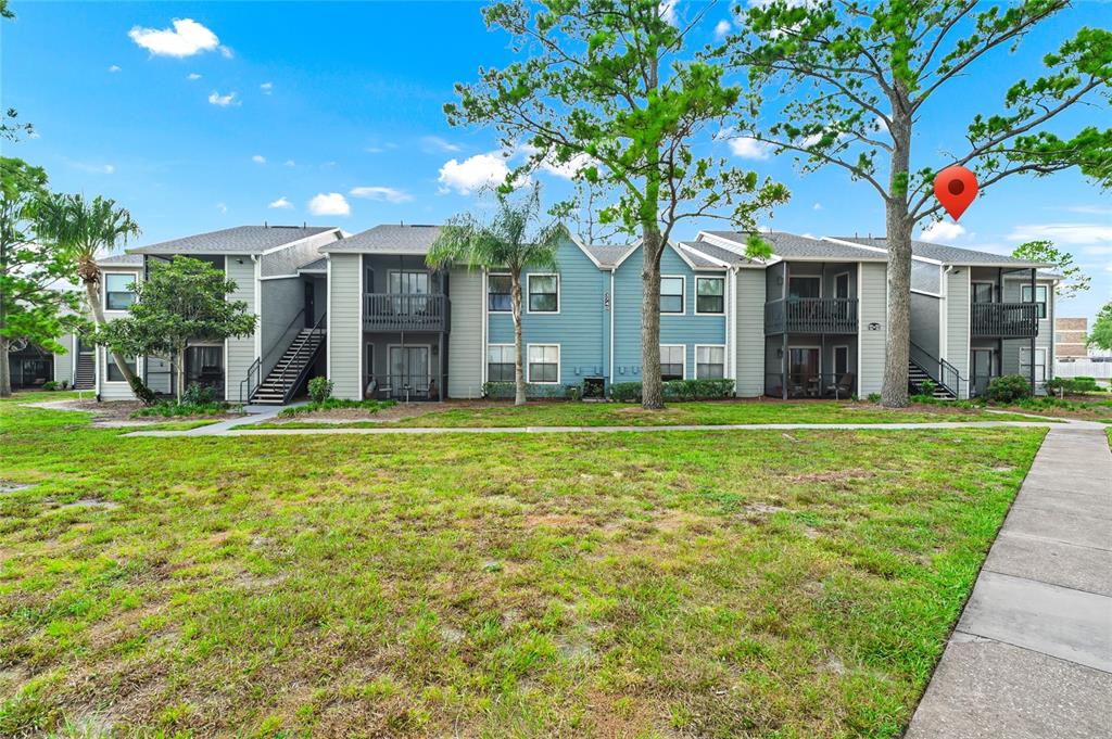A multi-story apartment building with gray and blue siding stands behind a grassy lawn — 3740 IDLEBROOK CIRCLE UNIT 102, CASSELBERRY, FL