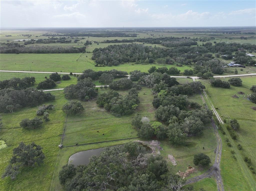 An aerial view shows a large, grassy rural property with scattered trees and a pond — 14935 COKER GULLY ROAD, MYAKKA CITY, FL