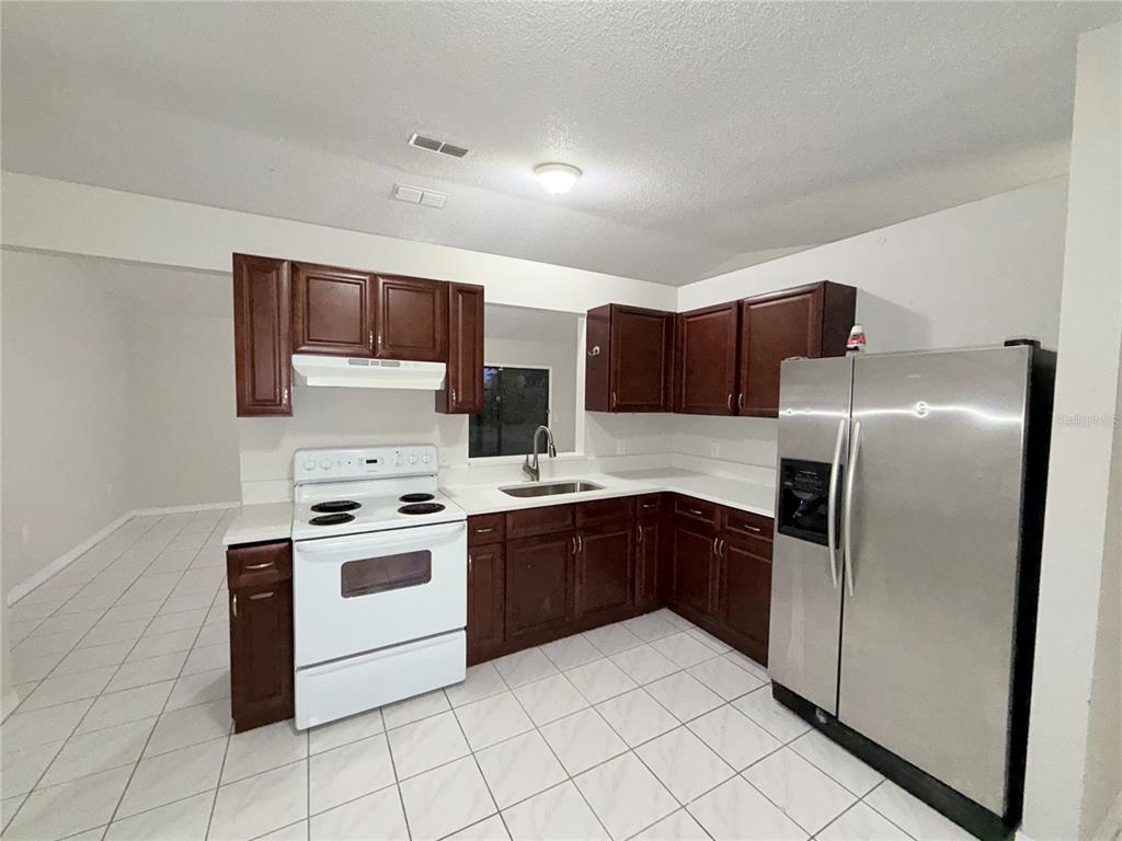 A kitchen features dark wood cabinets, white countertops, a white stove, and a stainless refrigerator — 2873 COTTONDALE DRIVE, DELTONA, FL