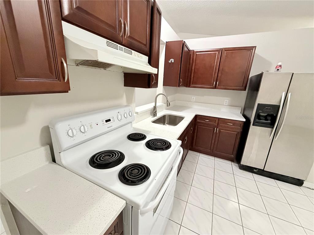 A kitchen features dark wood cabinets, white countertops, a white electric stove, and tile flooring — 2873 COTTONDALE DRIVE, DELTONA, FL