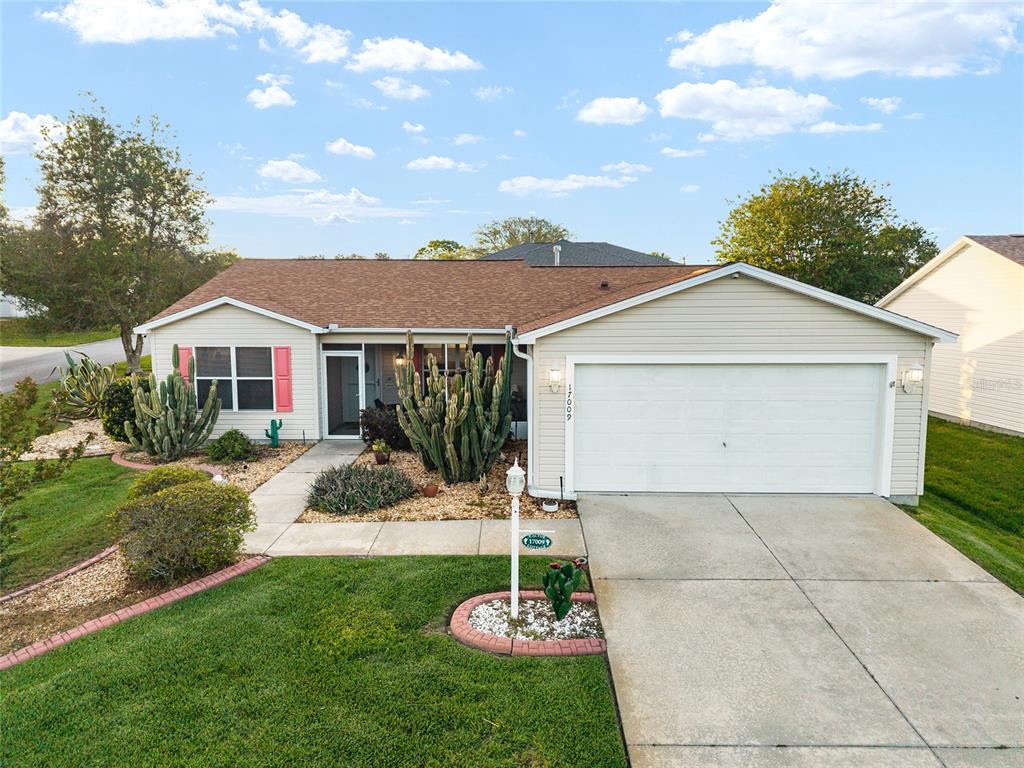 A single-story house with beige siding, a two-car garage, and a landscaped front yard — 17009 SE 96TH CHAPELWOOD CIRCLE, THE VILLAGES, FL