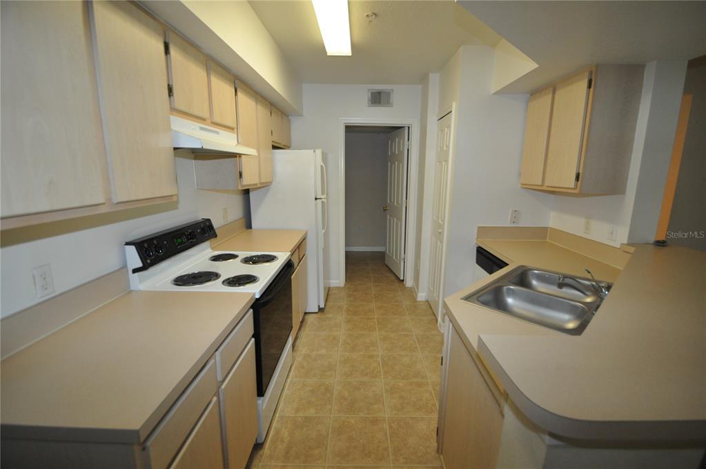 A galley-style kitchen features light wood cabinets, beige laminate countertops, and white appliances — 738 CREST PINES DRIVE UNIT 734, ORLANDO, FL