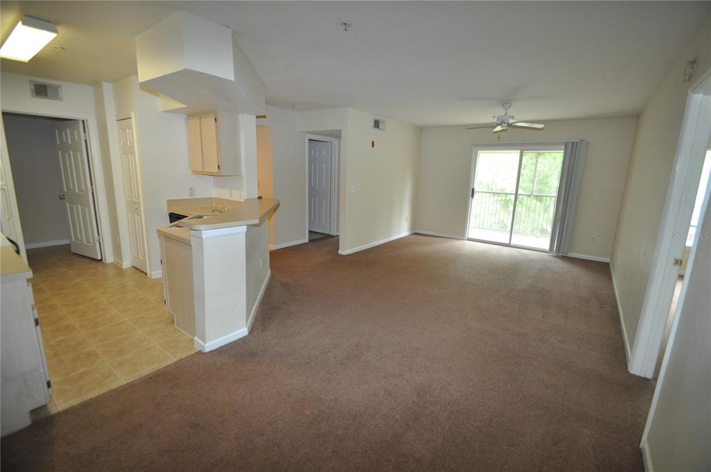 An open-concept living area with brown carpeting, a kitchen counter, and a sliding glass door — 738 CREST PINES DRIVE UNIT 734, ORLANDO, FL