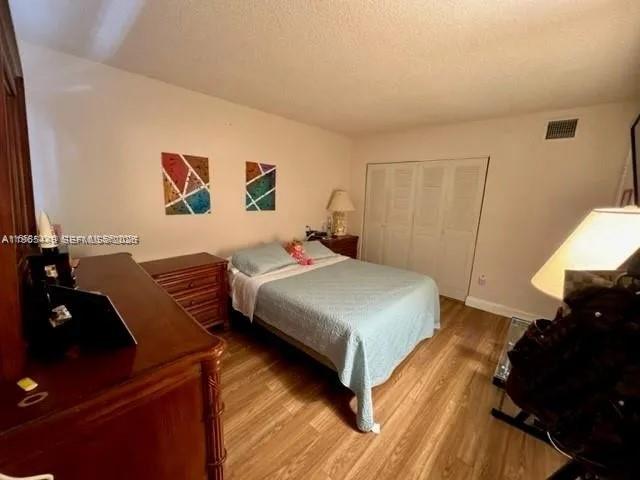 A bedroom features a bed with a light blue quilt, wood flooring, and white walls — 1840 Dewey St # 103, Hollywood FL 33020, HOLLYWOOD, FL